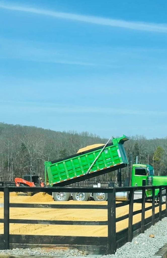 Green Peterbilt dump truck dumping sand near a fence line
