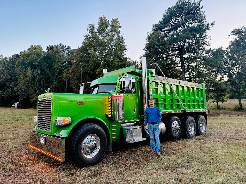 Andrew Pulaski standing in front of his green Peterbilt dump truck