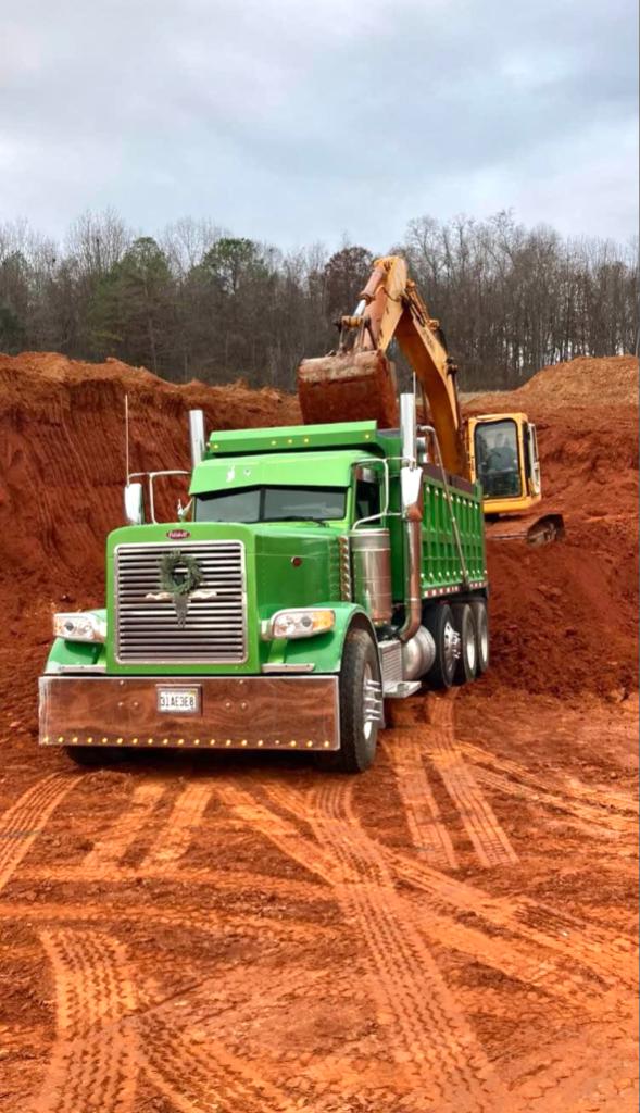 Excavator loading chert into a green Peterbilt dump truck on a job site